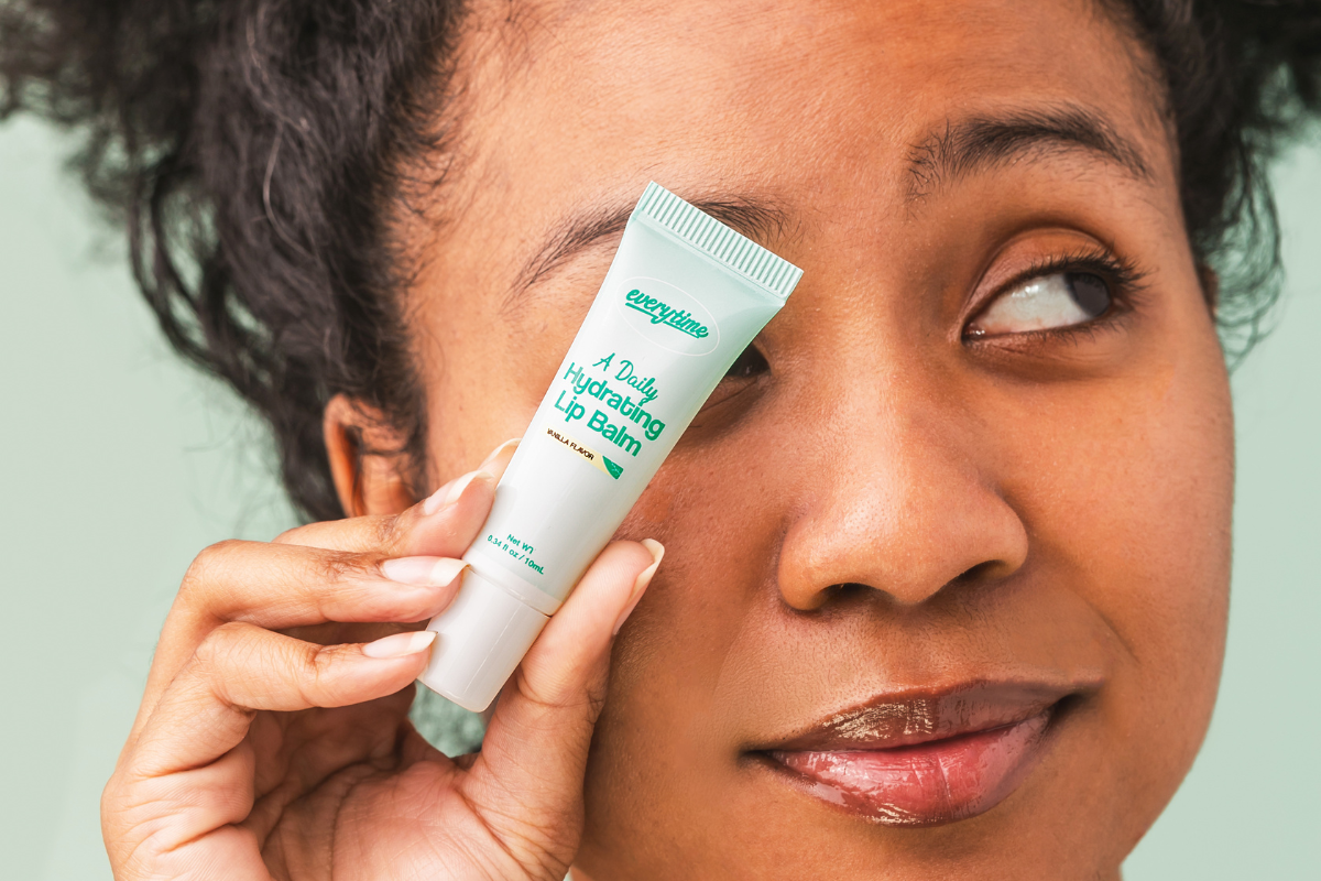 Playful pose with model showing Everytime lip balm and soft, glowing lips